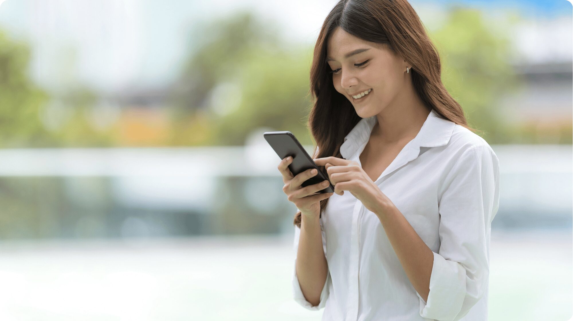 Woman with long brown hair wearing a white shirt reviewing something on her mobile and smiling.