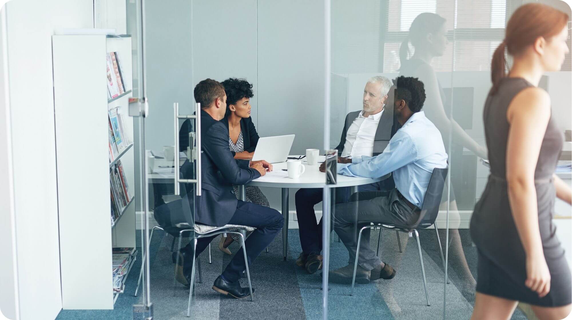 There are four colleagues sat around a circular table in a meeting style setting within an office.