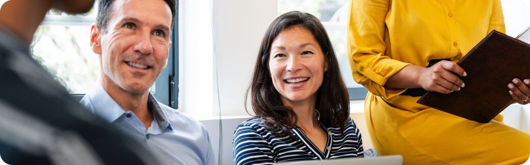 A group of people are sat together looking happy in a meeting style setting.