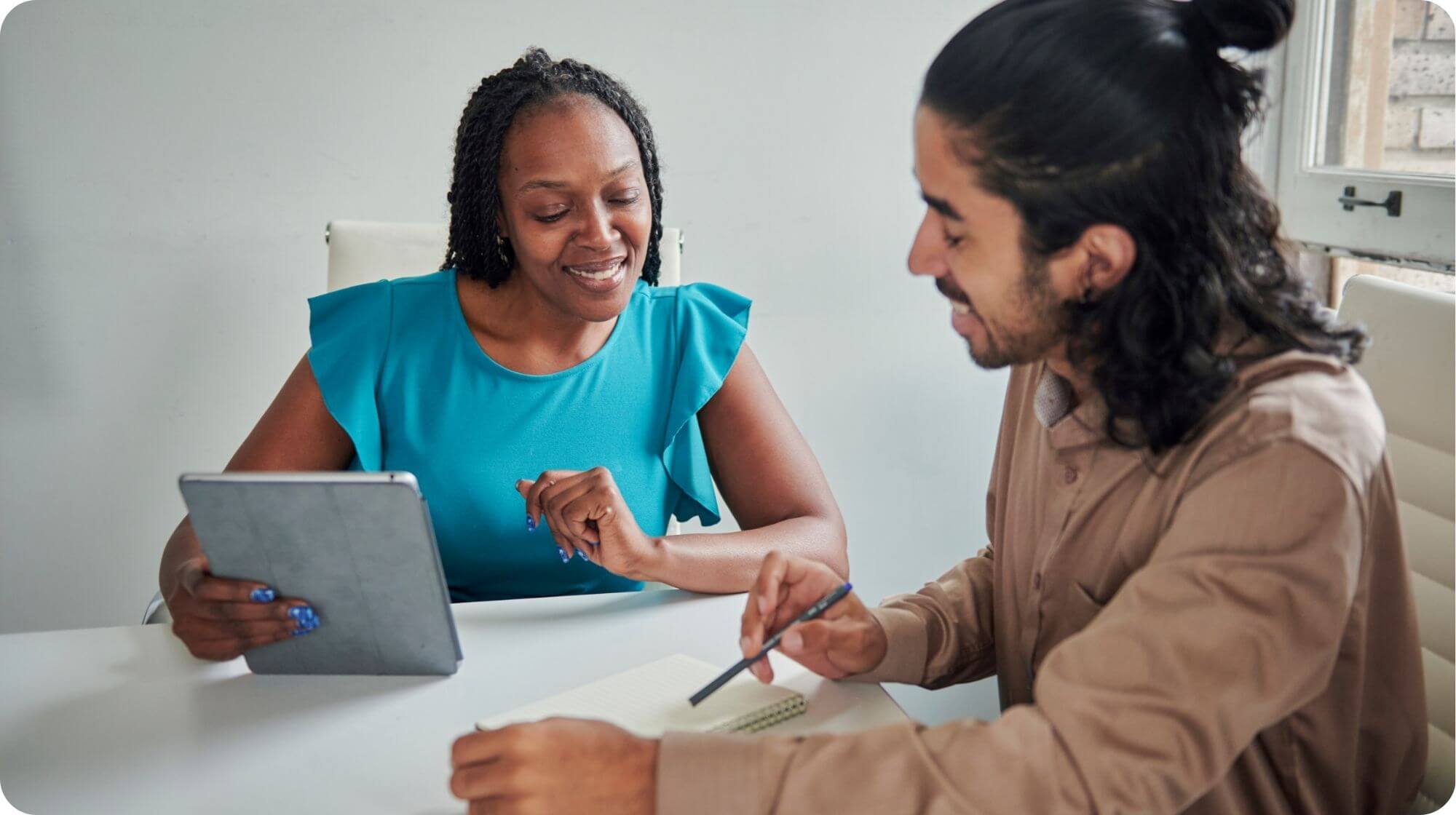 Two people are sat at a desk smiling and reviewing a notepad.